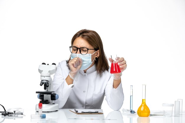 Vue de face femme médecin en costume médical blanc avec masque en raison de la toux covid sur l'espace blanc