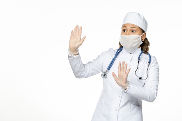 Vue de face femme médecin en costume médical blanc et portant un masque en raison d'un coronavirus sur l'isolement de la maladie pandémique de bureau blanc Covid