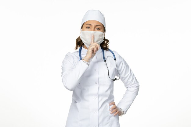 Vue de face femme médecin en costume médical blanc et portant un masque en raison d'un coronavirus sur sol blanc isolement de la maladie pandémique Covid