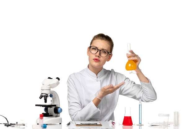 Vue de face femme médecin en costume médical blanc travaillant avec des solutions sur un bureau blanc