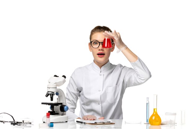 Vue de face femme médecin en costume médical blanc travaillant avec des solutions sur un bureau blanc