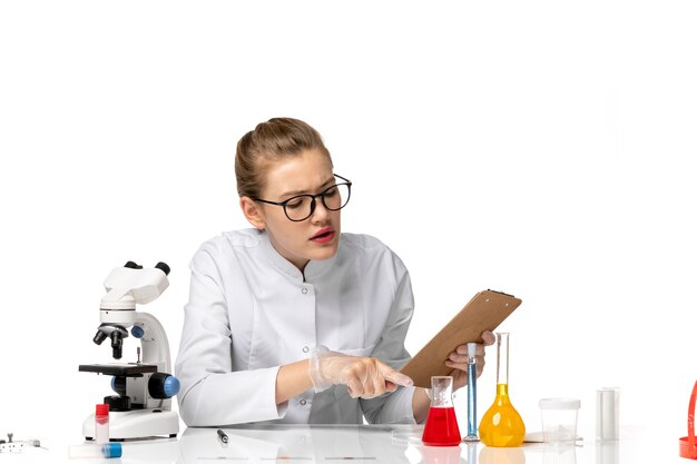 Vue de face femme médecin en costume médical blanc travaillant avec des solutions sur un bureau blanc