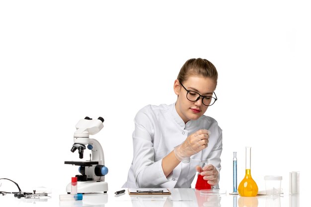 Vue de face femme médecin en costume médical blanc travaillant avec des solutions sur un bureau blanc