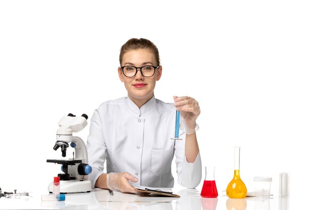 Vue de face femme médecin en costume médical blanc travaillant avec des solutions sur l'espace blanc