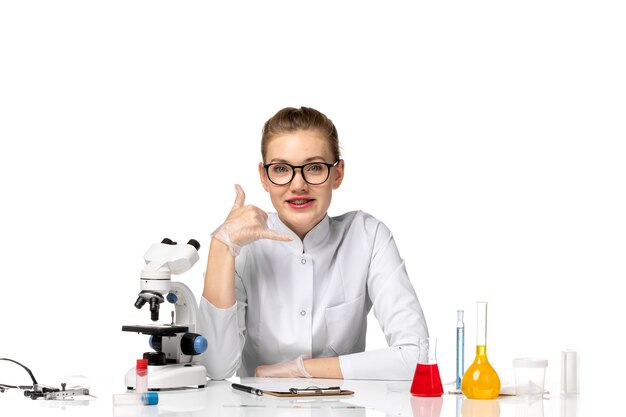 Vue de face femme médecin en costume médical avec des gants assis avec des solutions sur l'espace blanc