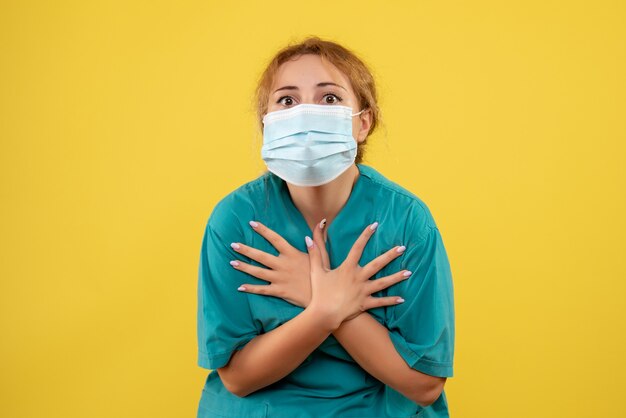 Vue de face de la femme médecin en costume médical et masque sur mur jaune