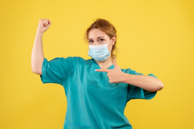 Vue de face de la femme médecin en costume médical et masque sur mur jaune