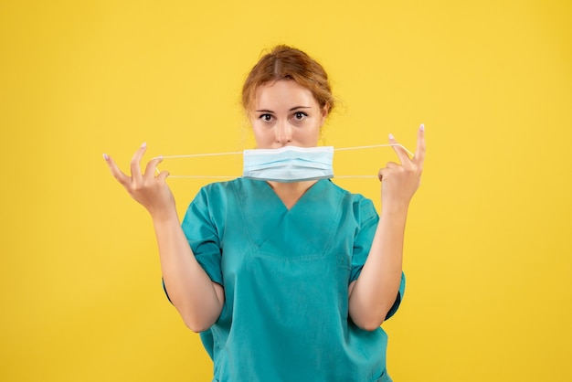 Vue de face de la femme médecin en costume médical et masque sur mur jaune