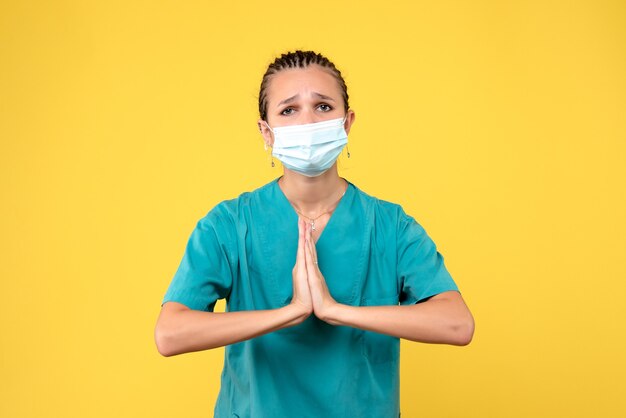 Vue de face de la femme médecin en costume médical et masque stérile sur mur jaune