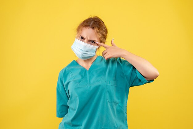 Vue de face de la femme médecin en costume médical et masque stérile sur mur jaune