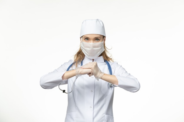 Vue de face femme médecin en costume médical avec masque stérile en raison d'un coronavirus sur la santé pandémique de la maladie du mur blanc