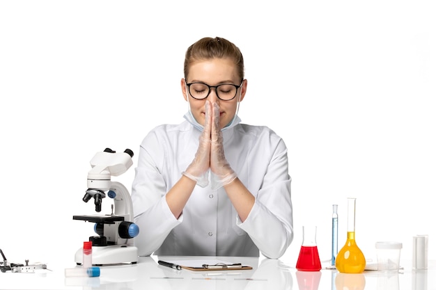 Vue de face femme médecin en costume médical avec masque stérile en raison de covid sur un bureau blanc