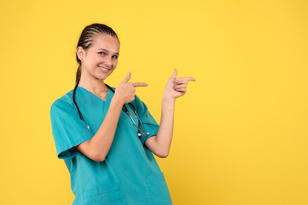 Vue de face de la femme médecin en costume médical sur le mur jaune