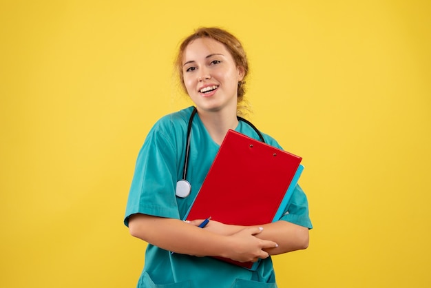 Vue de face de la femme médecin en costume médical avec papiers et analyse sur mur jaune