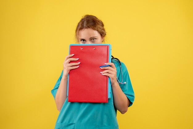 Vue de face de la femme médecin en costume médical avec papiers et analyse sur mur jaune