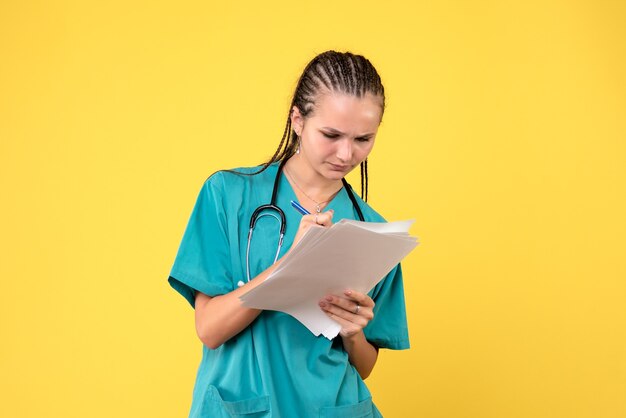 Vue de face de la femme médecin en costume médical avec des papiers sur mur jaune