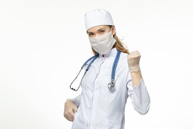 Vue de face femme médecin en costume médical portant un masque en raison d'un coronavirus sur le virus de la maladie de bureau blanc covid- maladie de la maladie pandémique