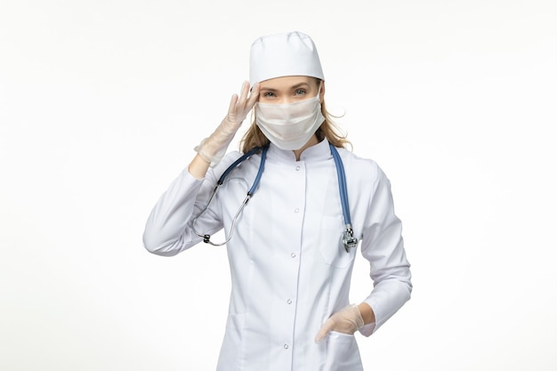 Vue de face femme médecin en costume médical portant un masque en raison de la pensée du coronavirus sur la maladie du mur blanc virus covid- maladie de la maladie pandémique