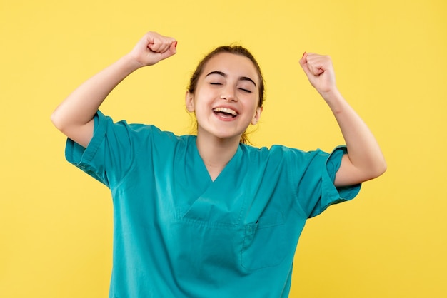 Vue de face de la femme médecin en costume médical se réjouissant avec le visage ravi sur le mur jaune