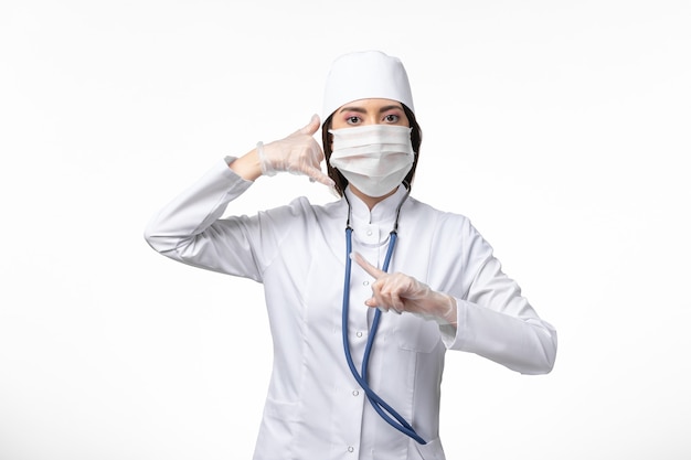 Vue de face femme médecin en costume médical stérile blanc avec masque en raison d'un coronavirus sur un mur blanc clair maladie pandémique maladie covid- virus