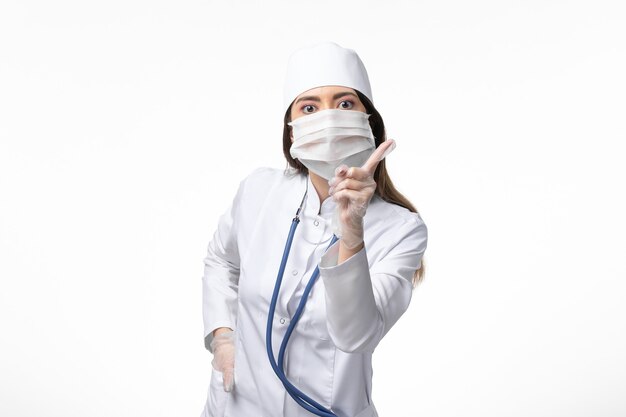 Vue de face femme médecin en costume médical stérile blanc avec masque en raison d'un coronavirus sur le mur blanc maladie covid- virus de la maladie pandémique