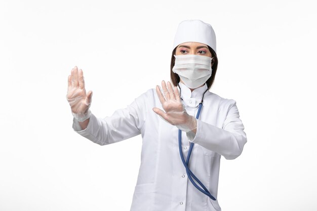 Vue de face femme médecin en costume médical stérile blanc avec masque en raison d'un coronavirus sur le mur blanc maladie pandémique maladie virus covid-