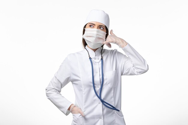Vue de face femme médecin en costume médical stérile blanc avec masque en raison du coronavirus sur la maladie du mur blanc maladie pandémique covid- virus