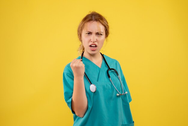 Vue de face de la femme médecin en costume médical avec stéthoscope sur mur jaune