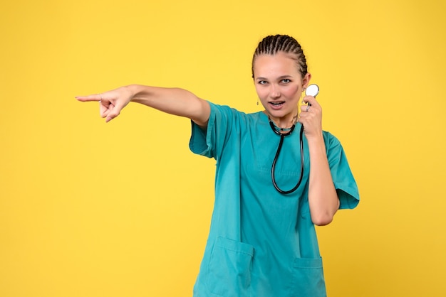 Vue de face de la femme médecin en costume médical avec stéthoscope sur mur jaune