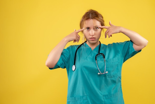 Vue de face de la femme médecin en costume médical avec stéthoscope sur mur jaune