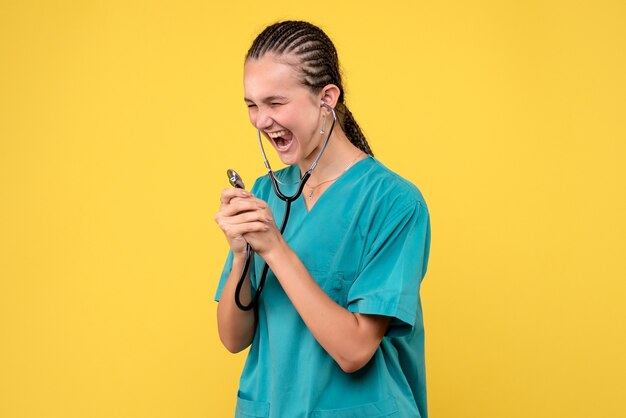 Vue de face de la femme médecin en costume médical avec stéthoscope sur mur jaune