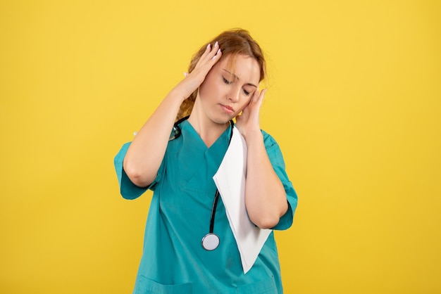 Vue de face de la femme médecin en costume médical tenant l'analyse sur mur jaune