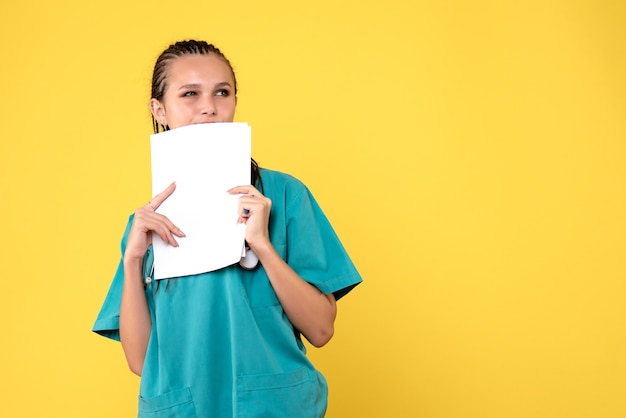 Photo gratuite vue de face de la femme médecin en costume médical tenant des papiers sur mur jaune