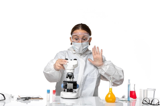Vue de face femme médecin en costume spécial et portant un masque travaillant avec un microscope sur fond blanc virus coronavirus pandémique covid