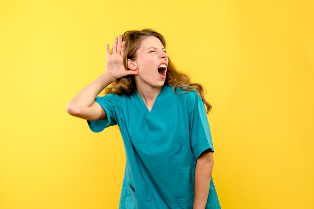 Vue de face de la femme médecin à l'écoute sur le mur jaune