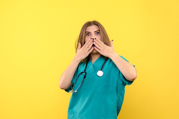 Vue de face de femme médecin avec expression choquée sur mur jaune