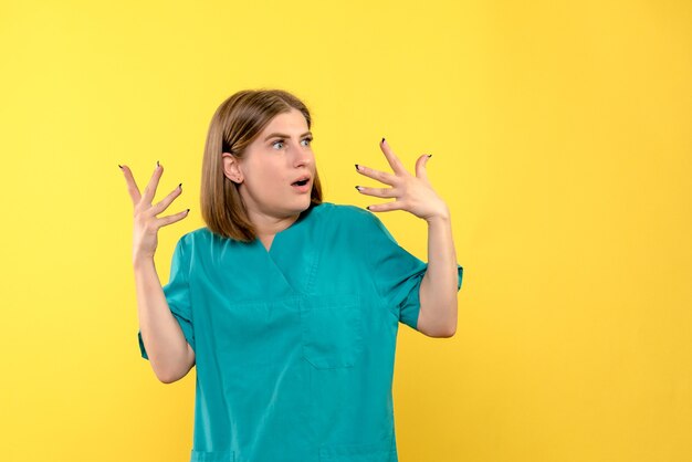 Vue de face de femme médecin avec expression surprise sur mur jaune