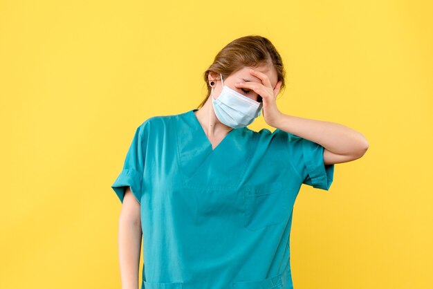 Vue de face femme médecin fatigué de travailler sur fond jaune maladie hospitalière covid- pandémie