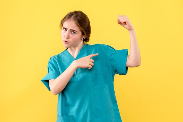 Vue de face femme médecin fléchissant sur fond jaune médical émotion santé hôpital