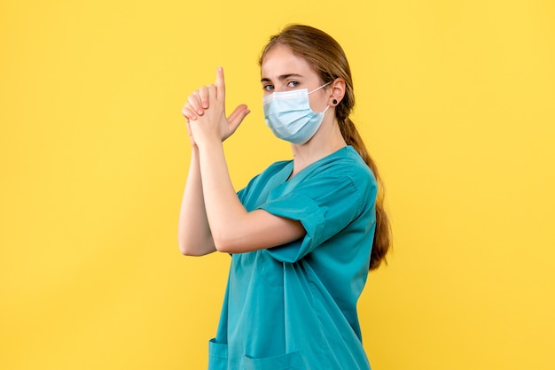 Vue de face femme médecin imitant le pistolet tenant sur fond jaune la santé de l'hôpital covid-