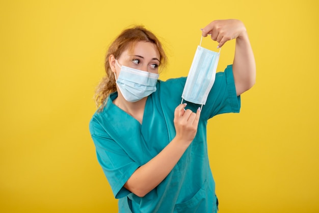 Vue de face femme médecin en masque de chemise médicale et tenant un autre masque, pandémie d'émotion de la santé du virus covid-19 de couleur