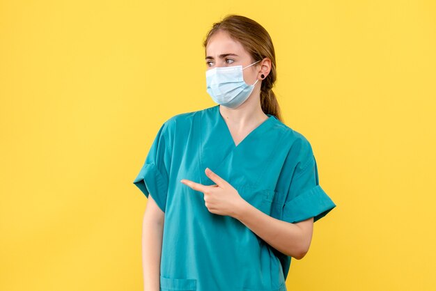 Vue de face femme médecin en masque sur fond jaune - pandémie hôpital covid