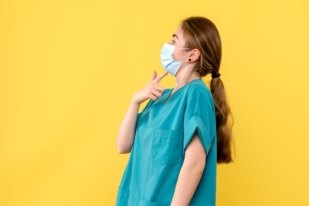 Vue de face femme médecin en masque sur fond jaune pandémie de l'hôpital de santé covid