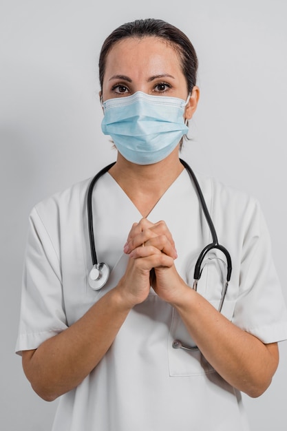 Vue de face de la femme médecin avec masque médical et stéthoscope priant