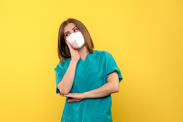 Vue de face de femme médecin avec masque sur mur jaune