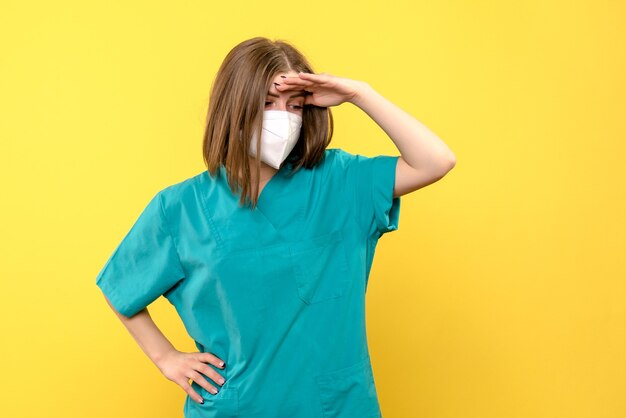 Vue de face de femme médecin avec masque sur mur jaune