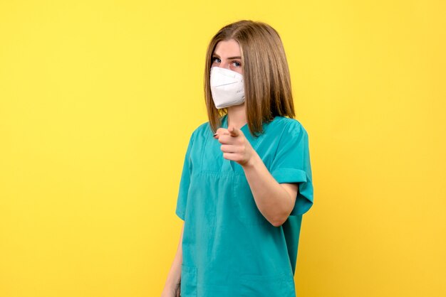 Vue de face de femme médecin avec masque sur mur jaune