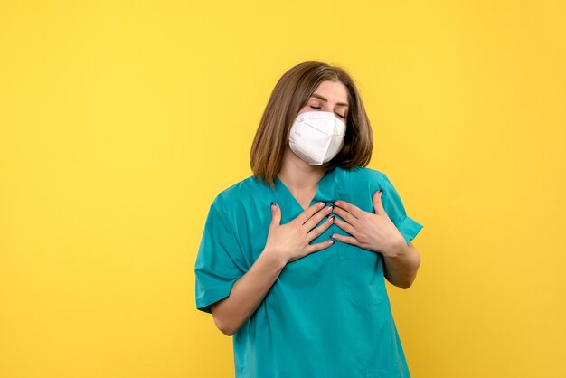 Vue de face de femme médecin avec masque sur mur jaune