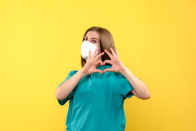 Vue de face de femme médecin avec masque sur mur jaune