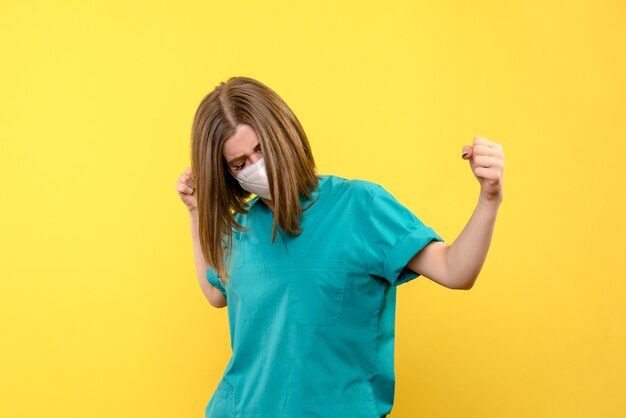 Vue de face de femme médecin avec masque sur mur jaune